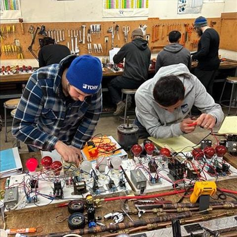 Hands-on HVAC electrical training board with students wiring components